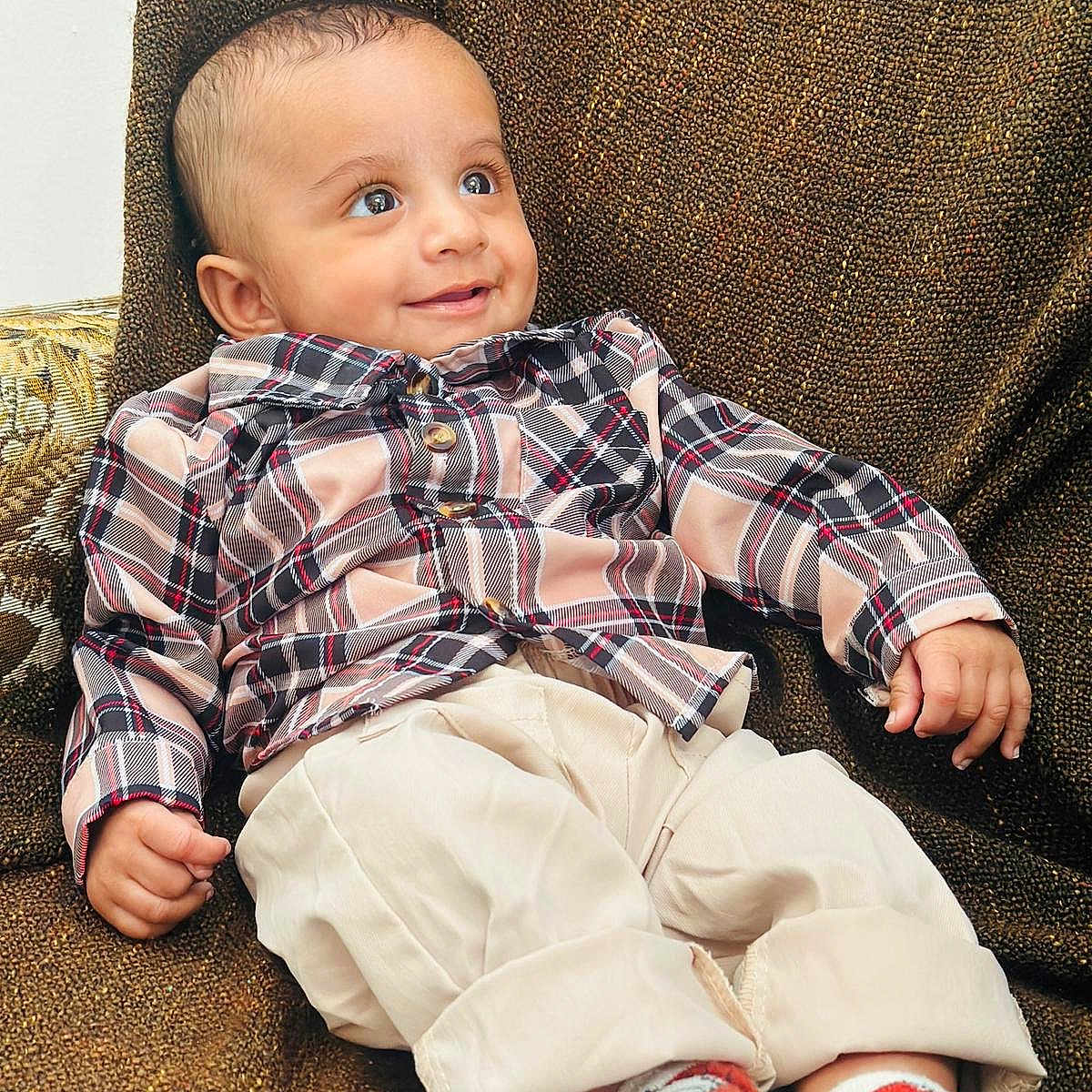 Navdeep is registered to the contest to win money with this photo: baby, beige_pants, bright_eyes, casual_clothing, chair, child, cute, furniture, happy, indoor, infant, plaid_shirt, portrait, relaxed, seated, small_hands, smiling, socks, texture, young_child