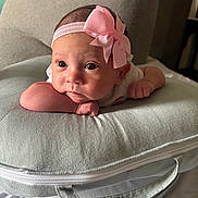 Eleanna is registered to the contest to win money with this photo: baby, infant, headband, pink_bow, cushion, gray, soft, face, portrait, child, cute, resting, indoors, closeup, newborn, person, expression, skin, small_hands, lying_down