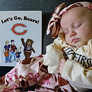 Lucy is registered to the contest to win money with this photo: baby, blanket, book, bow, chicago_bears, closeup, clothing, couch, face, fan, football, headband, indoors, infant, newborn, peaceful, portrait, sleeping, sports, swaddle