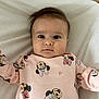 baby, infant, child, onesie, pink_clothing, minnie_mouse, blanket, lying_down, face, wide_eyes, cute, portrait, soft_texture, indoor, person, head, expression, young_child, sleepwear, toddler