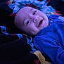baby, blanket, blue_clothing, child, closeup, cozy, cute, dimples, face, happy, indoor, infant, lying_down, patterned_blanket, person, portrait, sleepwear, smiling, soft_lighting, warmth