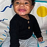 baby, smiling, child, sitting, black_sweater, gray_pants, curly_hair, play_mat, colorful_background, happy, indoors, cute, portrait, young_child, person, infant, one_person, bright, cozy, buttoned_clothing