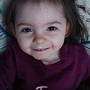 Elora a rejoint le concours — aidez-le/la à gagner de superbes lots ! child, clothing, cute, eyes, face, girl, hair, happy, indoors, patterned_background, person, pillow, ponytail, portrait, purple_shirt, sitting, skin, smile, toddler, young