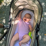 Ayla is registered to the contest to win money with this photo: baby, stroller, infant, onesie, outdoor, gravel, sunlight, shadow, leaf, happy, smiling, toy, green, person, footwear, shoe, sock, leg, hand, nature