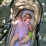 baby, stroller, infant, onesie, outdoor, gravel, sunlight, shadow, leaf, happy, smiling, toy, green, person, footwear, shoe, sock, leg, hand, nature