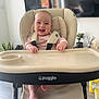 Ayla is registered to the contest to win money with this photo: baby, high_chair, smiling, indoor, infant, face, feet, furniture, plant, television, window, wood_floor, clothing, seatbelt, table, happy, person, child, home, cute