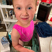Amara is registered to the contest to win money with this photo: child, pink_clothing, face, smile, bathroom, step_stool, towel, counter, toiletries, floor, person, indoors, expression, skin, hair, arm, hand, cabinet, sink, appliance
