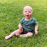 Phoenix joined the competition — help win amazing prizes! baby, child, grass, outdoor, smiling, happy, sitting, green_shirt, shorts, barefoot, nature, lawn, cute, infant, playful, summer, sunlight, portrait, one_person, casual