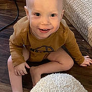 Phoenix joined the competition — help win amazing prizes! barefoot, brown_clothing, child, cushion, eyes, face, floor, foot, hand, happy, home, indoor, patterned_cushion, person, rug, sitting, smile, sweater, toddler, wooden_floor
