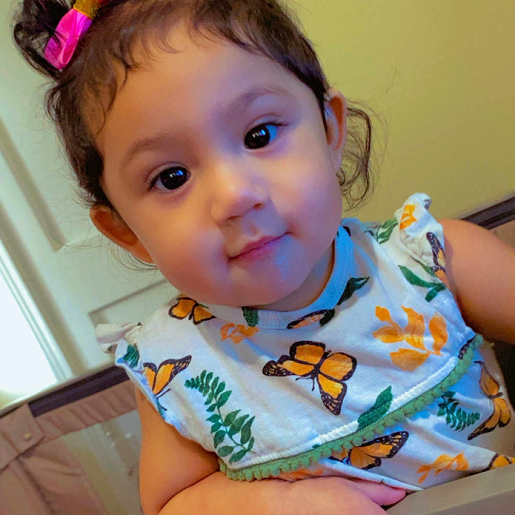 Azariah Estrada is registered to the contest to win money with this photo: toddler, child, baby, face, smile, bow, hair, dress, butterfly_print, hand, crib, indoor, person, cute, young_child, curly_hair, colorful, happy, portrait, home