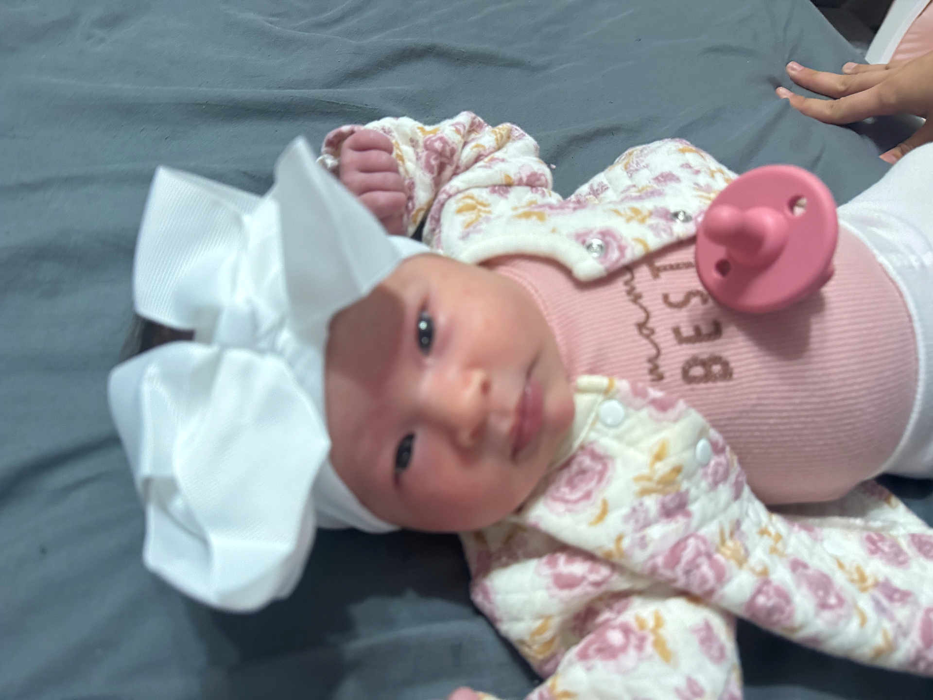 Ashanti Dafne joined the competition — help win amazing prizes! baby, headwear, bow, pacifier, pink_clothing, floral_jacket, hands, gray_background, infant, lying_down, child, indoors, cute, portrait, soft_toys, human, newborn, sleepwear, small_hands, closeup
