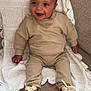baby, child, smiling, sitting, beige_clothing, sneakers, blanket, couch, knitted_blanket, happy, indoors, person, footwear, casual_wear, cute, young_child, infant, portrait, home, cozy