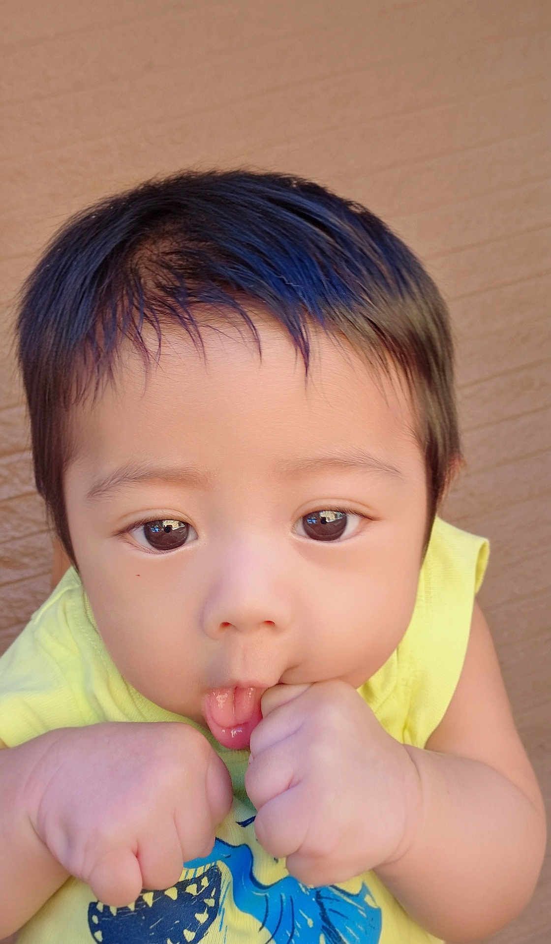 Yesu joined the competition — help win amazing prizes! baby, blue_graphic, child, closeup, curly_hair, cute, expression, eyes, face, fist, hand, indoor, infant, person, playful, portrait, skin, sucking, yellow_shirt, young_child