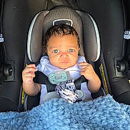Jaxon is registered to the contest to win money with this photo: baby, car_seat, blanket, pacifier, child, infant, seatbelt, blue, curly_hair, expression, person, indoors, cushion, clothing, cute, small_hands, portrait, head, face, safety