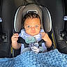 baby, car_seat, blanket, pacifier, child, infant, seatbelt, blue, curly_hair, expression, person, indoors, cushion, clothing, cute, small_hands, portrait, head, face, safety
