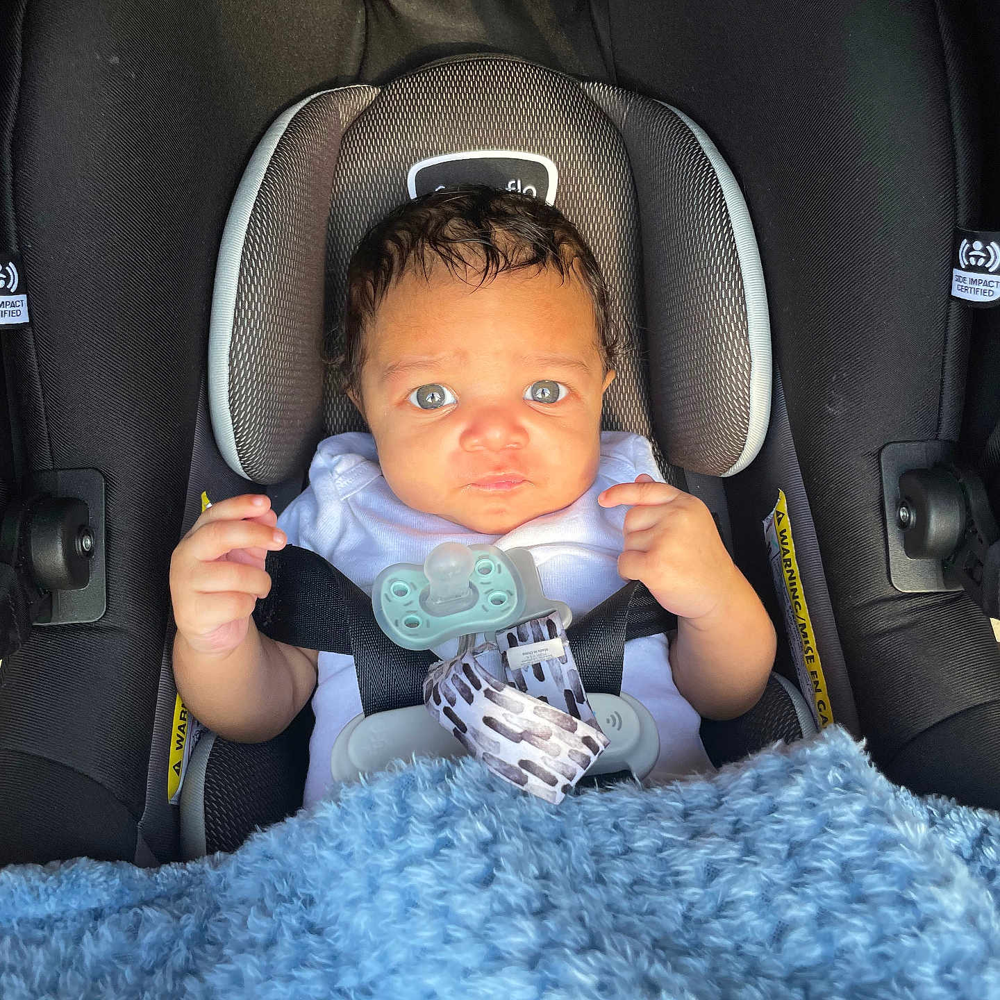 Jaxon is registered to the contest to win money with this photo: baby, car_seat, blanket, pacifier, child, infant, seatbelt, blue, curly_hair, expression, person, indoors, cushion, clothing, cute, small_hands, portrait, head, face, safety