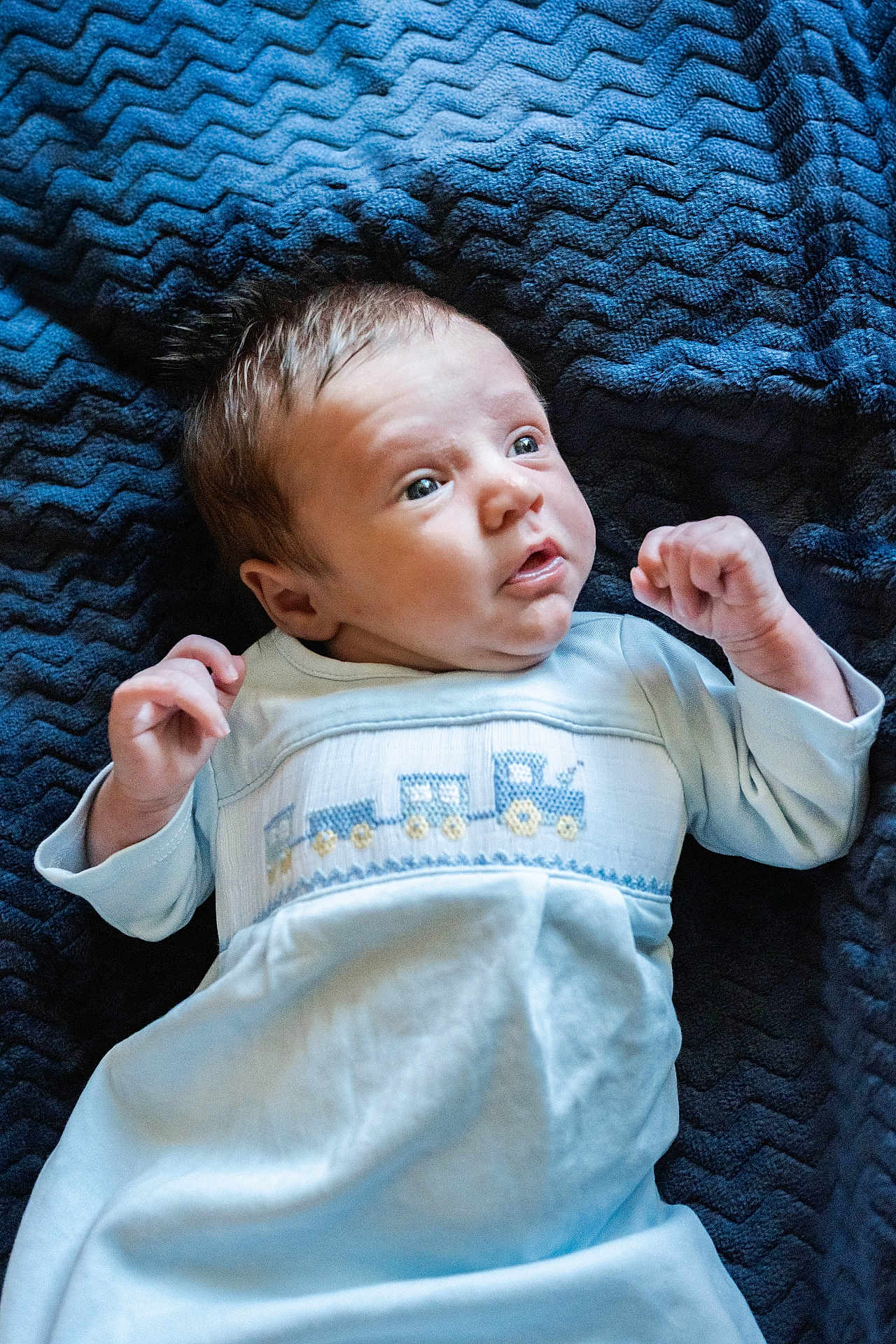 Sawyer joined the competition — help win amazing prizes! baby, infant, newborn, blanket, bedding, blue_blanket, onesie, clothing, face, eyes, hands, portrait, lying_down, soft_texture, cute, surprised_expression, gaze, hair, nursery, cozy