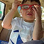 adjusting_glasses, blue_design, car_interior, casual, child, child_in_car, expression, face, glasses, hair, hand, playful, portrait, red_frames, seat, seatbelt, sunlight, white_tshirt, window, young