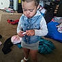 Debani is registered to the contest to win money with this photo: toddler, child, denim_vest, grey_skirt, white_sandals, carpet, living_room, clutter, person, bed, blanket, foot, phone, toy, indoor, furniture, curtains, socks, floor, casual