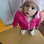 Debani is registered to the contest to win money with this photo: casual_clothing, child, cozy, curious, door, floor, indoor, knit_hat, looking_up, person, pink_hat, pink_jacket, pom_pom, shoes, standing, toddler, warm_clothing, white_door, wooden_floor, young_child