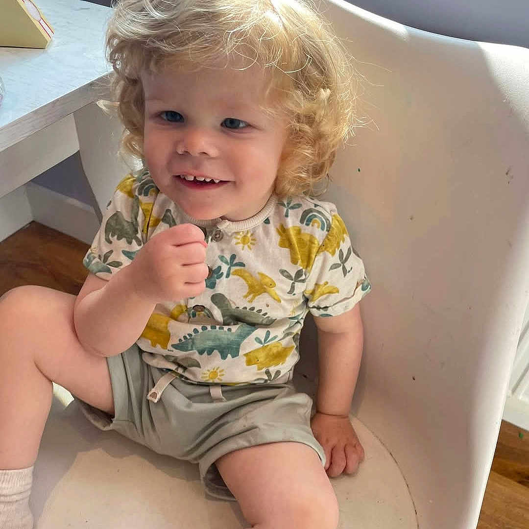Charlie is registered to the contest to win money with this photo: baby, blonde, clothing, cream, dessert, face, food, furniture, hair, happy, head, hosiery, person, photography, portrait, shorts, sitting, sleeve, smile, sock