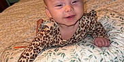 Maisey is registered to the contest to win money with this photo: baby, infant, smiling, bed, pillow, leopard_print, clothing, sleepy, room, bedroom, metal_bed_frame, floral_pattern, person, child, happy, lying_down, cozy, indoor, soft_lighting, cute