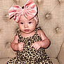 baby, child, toddler, pink_bow, headband, leopard_print, outfit, sitting, beige_chair, tufted_chair, furniture, cute, portrait, indoor, person, young_child, fashion, smiling, comfortable, cozy