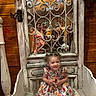 toddler, child, smiling, dress, floral, pigtails, bench, wood, mirror, reflection, metal_grille, vintage, family, indoor, wooden_wall, happy, people, portrait, seated, decor