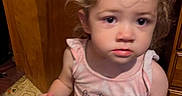Miah is registered to the contest to win money with this photo: child, toddler, indoor, curly_hair, snack, bag, wooden_door, cabinet, flooring, patterned_floor, pink_shirt, curious, blurry, person, young_child, standing, holding, expression, home, candid
