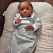 Peyton is registered to the contest to win money with this photo: baby, infant, child, face, expression, clothing, grey_outfit, cushion, soft, indoors, portrait, lying_down, cute, hands, head, skin, eyes, person, sleepwear, comfort