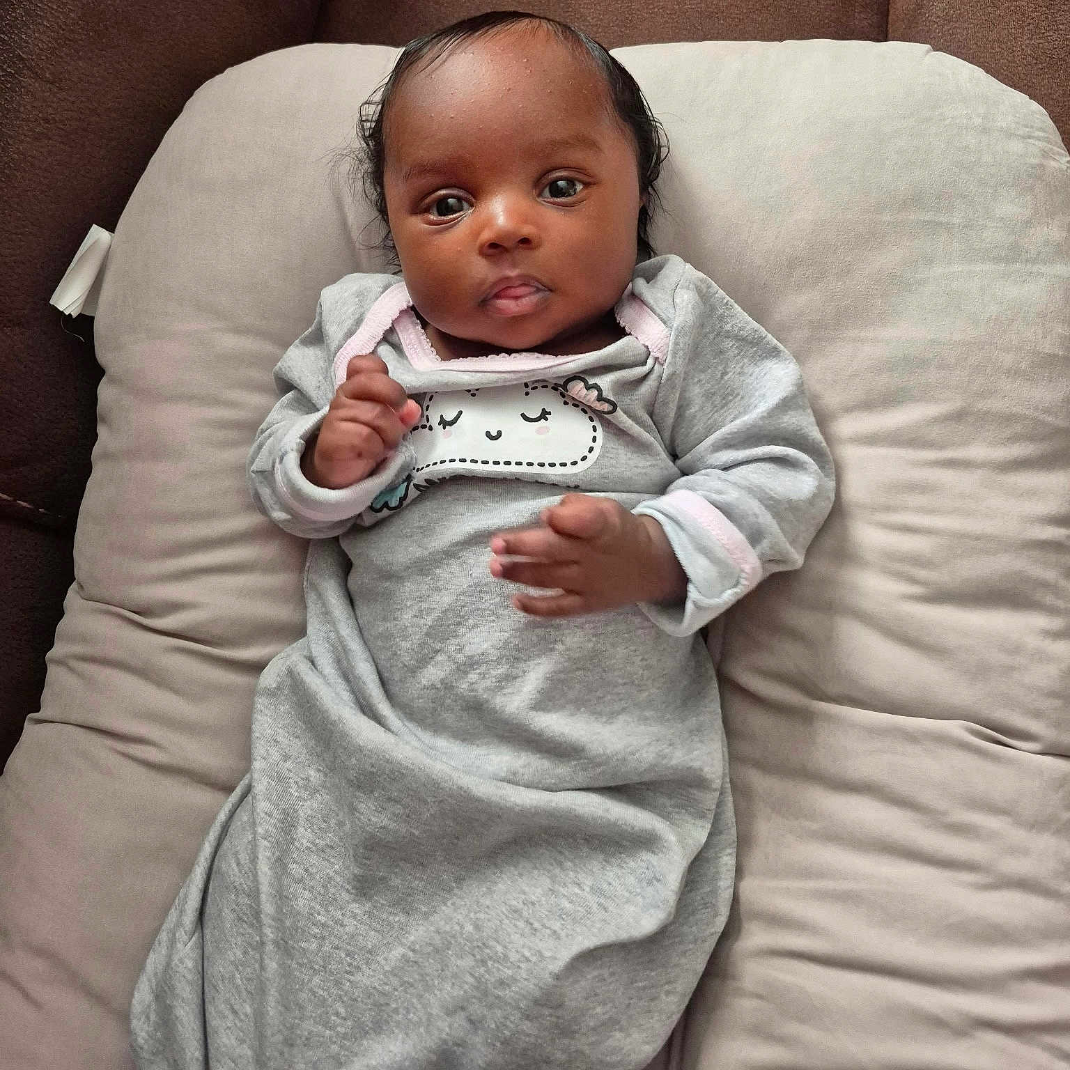 Peyton is registered to the contest to win money with this photo: baby, infant, child, face, expression, clothing, grey_outfit, cushion, soft, indoors, portrait, lying_down, cute, hands, head, skin, eyes, person, sleepwear, comfort