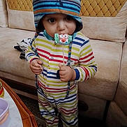Ilyes participe au concours pour gagner de l'argent avec cette photo : toddler, child, striped_clothing, hat, indoor, lollipop, candy, couch, furniture, person, face, eyes, hand, table, colorful, striped, cute, winter_hat, playful, standing