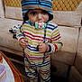 toddler, child, striped_clothing, hat, indoor, lollipop, candy, couch, furniture, person, face, eyes, hand, table, colorful, striped, cute, winter_hat, playful, standing