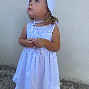 Lilou a rejoint le concours — aidez-le/la à gagner de superbes lots ! child, girl, white_dress, bonnet, curious, standing, outdoor, portrait, young_child, hands, expression, innocence, summer, footwear, wall, texture, looking_up, light_skin, blonde_hair, casual