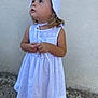 child, girl, white_dress, bonnet, curious, standing, outdoor, portrait, young_child, hands, expression, innocence, summer, footwear, wall, texture, looking_up, light_skin, blonde_hair, casual