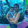 baby, child, woman, aquarium, fish, water, chain, tank, smile, holding, person, portrait, indoor, casual_clothing, shorts, tank_top, background, elderly_person, wheelchair, sign