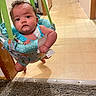 baby, blue_clothing, carpet, child, curiosity, curly_hair, doorway, expression, face, floor, home, indoor, infant, jumper, person, sitting, suspension, tag, tile_floor, wooden_door