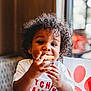 blurred_background, booth, child, curly_hair, cute, diner, eating, face, food, hands, happy, indoor, person, portrait, red_straw, snack, table, toddler, white_shirt, window