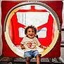 Noah joined the competition — help win amazing prizes! casual_clothing, child, curly_hair, cute, denim_shorts, fun, happy, indoor_playground, joyful, mesh_fence, play, play_structure, portrait, red_background, sitting, smiling, socks, toddler, white_tshirt, yellow_ring
