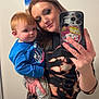 woman, toddler, child, selfie, mirror, phone, phone_case, hello_kitty, blue_shirt, tie_dye_clothing, tattoo, indoor, painting, art, casual_clothing, smile, holding, portrait, red_hair, happy