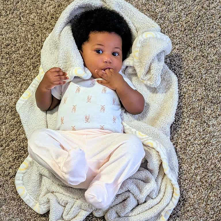 Cayra is registered to the contest to win money with this photo: baby, blanket, carpet, child, clothing, cozy, curious, curled_blanket, cute, expression, face, footed_pants, hand, indoor, infancy, infant, lying_down, person, soft_texture, toddler