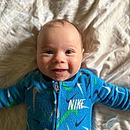 Ezio a rejoint le concours — aidez-le/la à gagner de superbes lots ! baby, smiling, blue_clothing, nike, onesie, infant, lying_down, blanket, happy, cute, child, face, portrait, indoors, soft_texture, patterned, young, person, casual, closeup