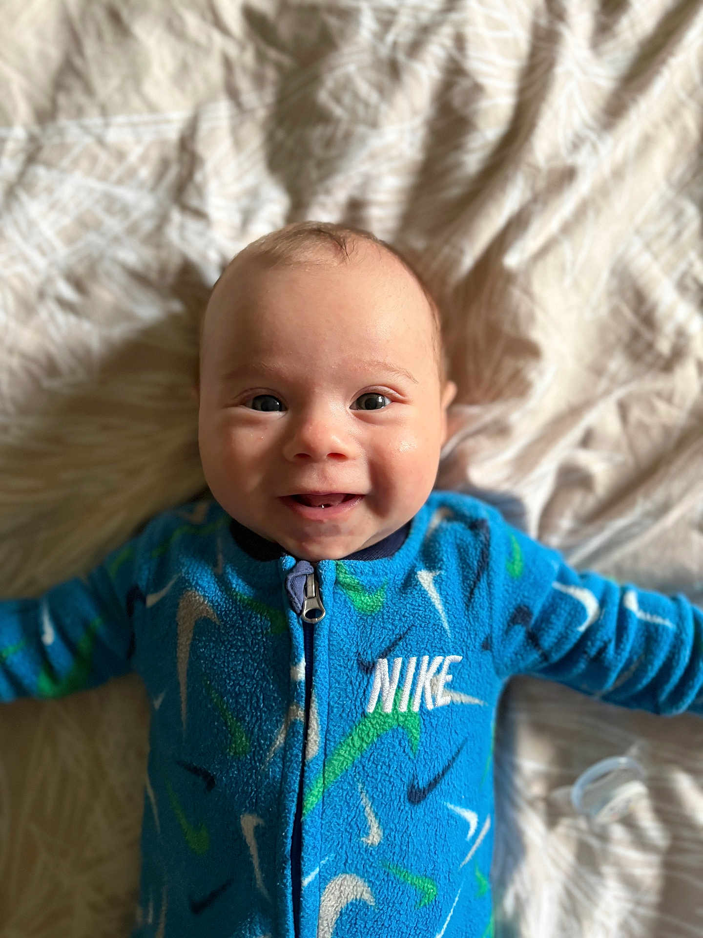 Ezio a rejoint le concours — aidez-le/la à gagner de superbes lots ! baby, smiling, blue_clothing, nike, onesie, infant, lying_down, blanket, happy, cute, child, face, portrait, indoors, soft_texture, patterned, young, person, casual, closeup