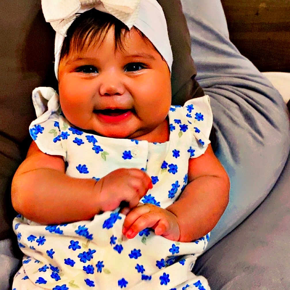 Mya Aylany joined the competition — help win amazing prizes! baby, blue_flowers, bow, child, chubby_cheeks, clothing, cushion, cute, cute_outfit, floral_outfit, gray, happy, headband, headwear, indoors, infant, person, portrait, sitting, smiling