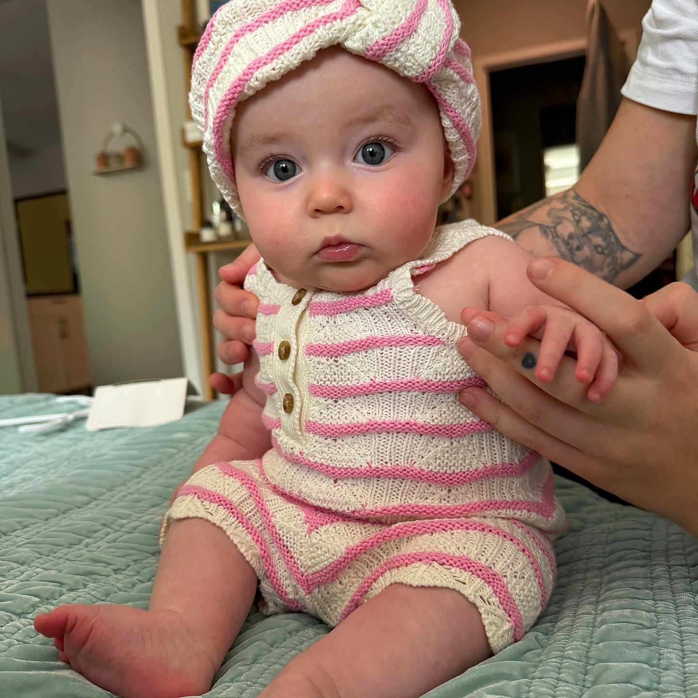Salem is registered to the contest to win money with this photo: baby, bed, blue_eyes, child, cozy, cute, hand, indoor, infant, knitwear, person, portrait, quilt, sitting, skin, soft_lighting, striped_clothing, supporting_hand, tattoo, turban