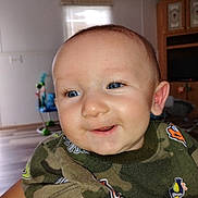 Mavrick joined the competition — help win amazing prizes! baby, child, face, smile, blue_eyes, indoor, camouflage, shirt, person, happy, closeup, infant, cute, expression, skin, head, young, eyelashes, background, furniture