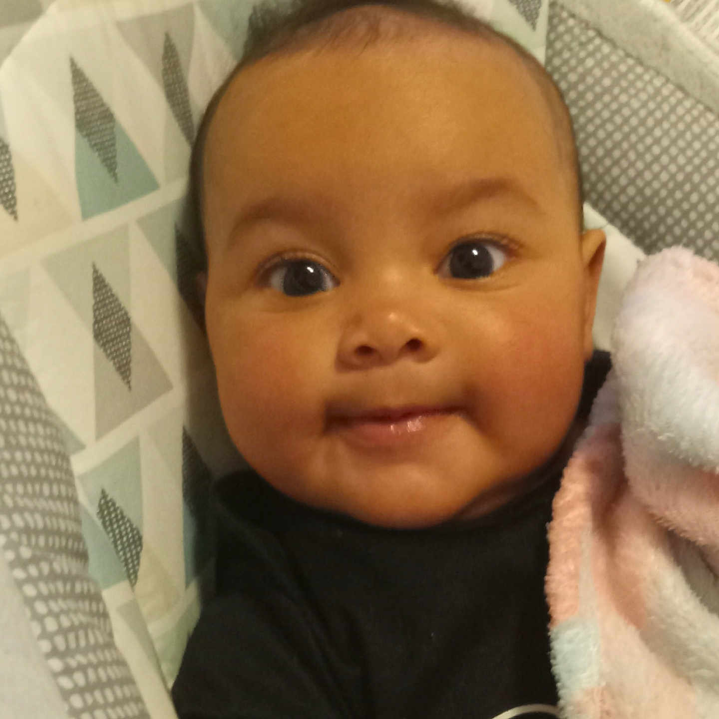 Yanny joined the competition — help win amazing prizes! baby, baby_seat, black_clothing, blanket, child, closeup, cozy, cute, eyes, face, happy, indoors, infant, patterned_background, person, portrait, smile, soft_texture, toddler, young