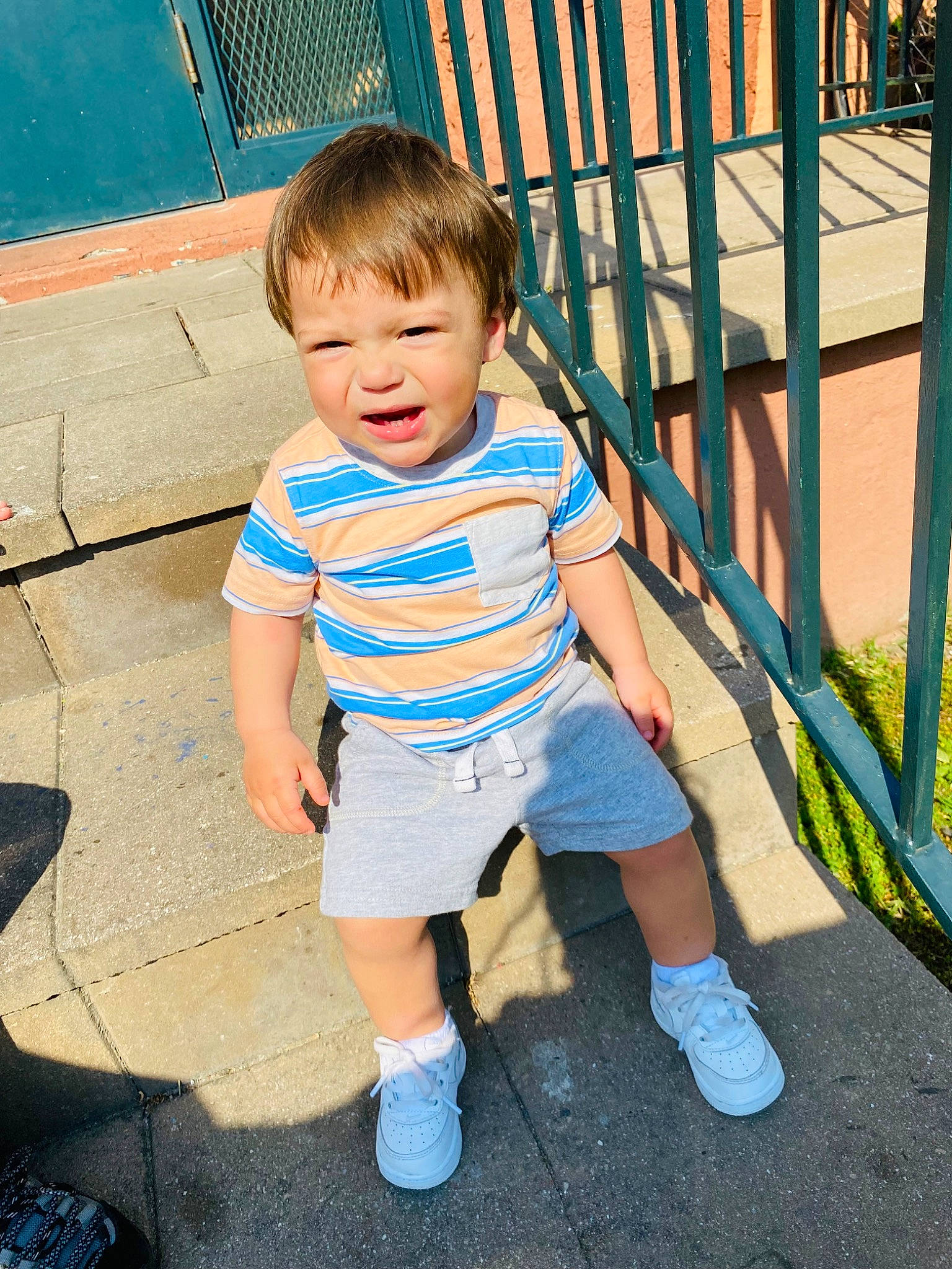 Amari is registered to the contest to win money with this photo: baby_toddler_clothing, child, cool, electric_blue, facial_expression, fence, fun, grass, hairstyle, happy, human_leg, leisure, people, person, public_space, shorts, smile, standing, summer, t_shirt