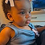 child, toddler, baby, curly_hair, ribbon, blue_tank_top, indoor, television, furniture, face, eyes, hand, skin, person, cute, portrait, clothing, sitting, expression, focus