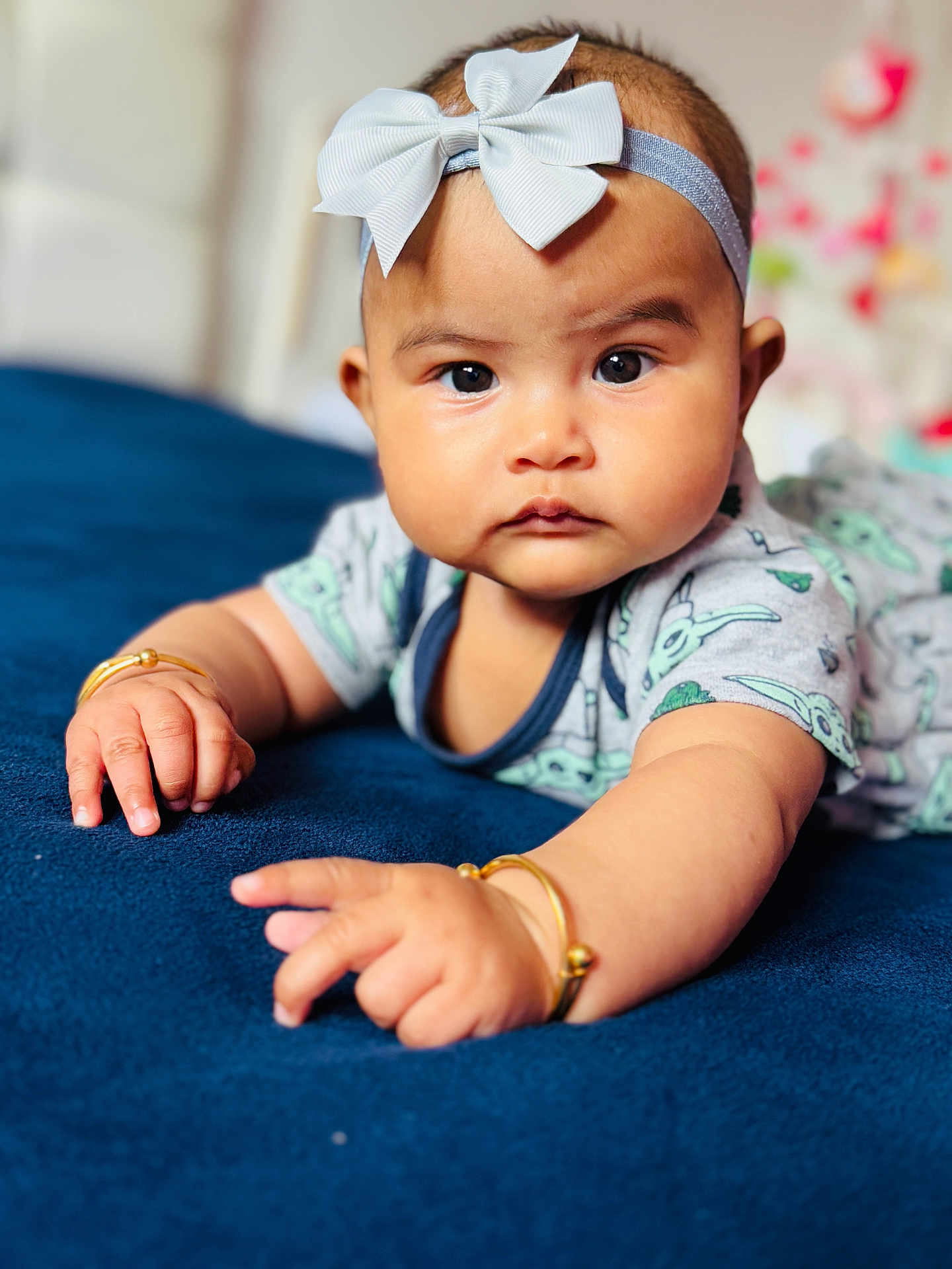 Ava joined the competition — help win amazing prizes! baby, child, infant, headband, bow, bracelet, hand, face, eyes, clothing, blue_blanket, soft_texture, portrait, closeup, indoors, curious, cute, decor, focus, expression